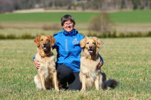 nainen ja kaksi koiraa istuvat nurmikolla kesällä